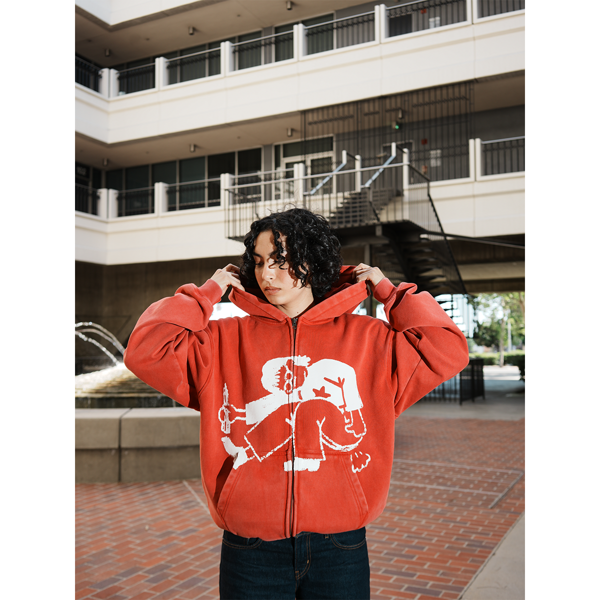 Model wearing a red hoodie with a graphic design in an outdoor setting